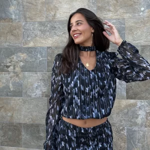 chica sonriendo delante de una pared con una blusa de gasa negra estampada blanco y celeste con choker en cuello del mismo tejido